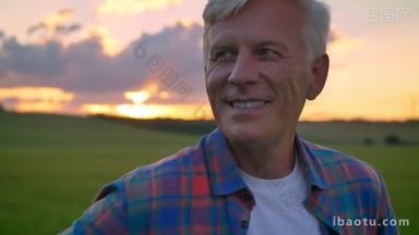 英俊的老人的肖像微笑着看着相机, 站在麦田, 美丽的景色与日落背景